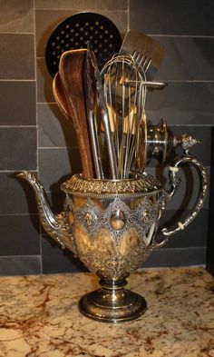 an ornate silver teapot with utensils in it on a marble counter top