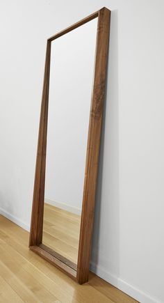 a large wooden mirror sitting on top of a hard wood floor next to a white wall