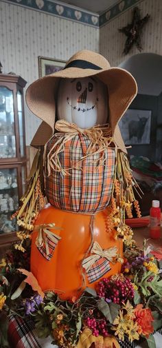 a scarecrow sitting on top of an orange pumpkin in a room with other decorations