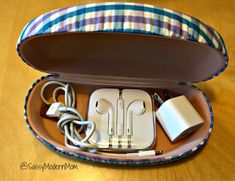 an open case with various items inside on a wooden table, including earphones and cords