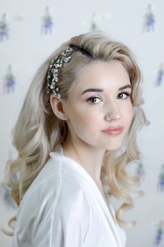 a woman with blonde hair wearing a white dress and a flower in her hair is looking at the camera