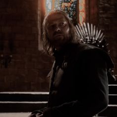 a man with long hair standing in front of a iron throne and looking at the camera