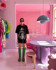 a woman standing in front of a pink room with clothes on the rack and table