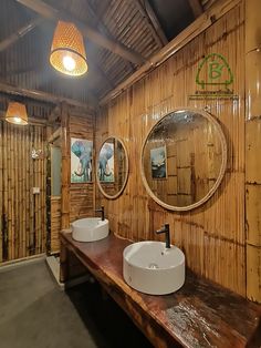 two sinks in a bamboo bathroom with round mirrors above them and lights hanging from the ceiling