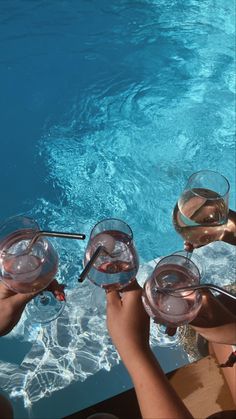 four people toasting with wine glasses in front of a swimming pool at the same time