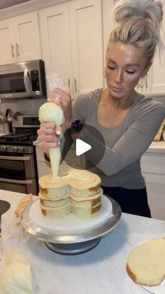 a woman is decorating a cake with white icing and butter on it in the kitchen