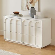 a white cabinet with two vases sitting on top of it next to a painting