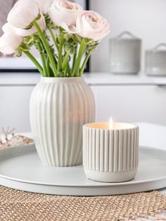 a white vase filled with flowers sitting on top of a table next to a lit candle