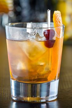 a close up of a drink with an orange peel on the rim and a cherry garnish