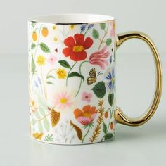 a white and gold coffee cup with flowers painted on the side, sitting on a table