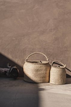 two baskets sitting next to each other on the ground near a wall with a shadow