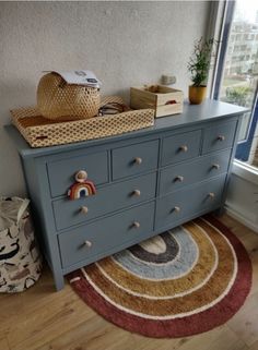 a dresser with drawers and baskets on top of it in front of a large window