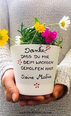 a person holding a flower pot with flowers in it that says danke des du mir