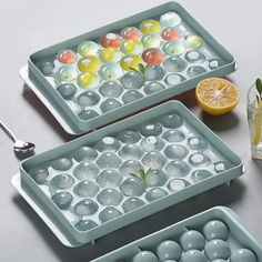 two serving trays filled with ice and lemon slices on a table next to an orange slice