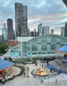 an amusement park with people and rides in front of the cityscape, as seen through a glass window