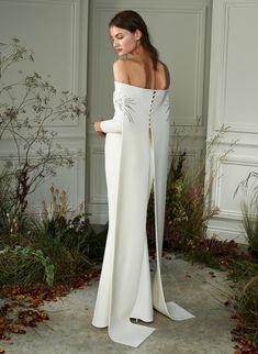 a woman standing in front of a wall wearing a white dress with an open back