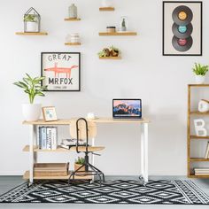 a desk with a laptop on it in front of some shelves and pictures hanging on the wall