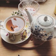 there is a tea pot and cup on the table next to each other with spoons