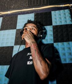 a man with headphones on his ears is singing into a microphone in front of a checkered wall