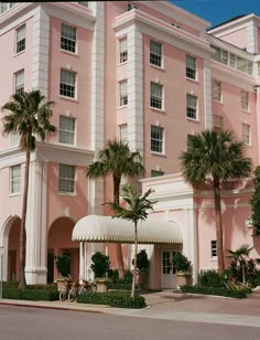 a large pink building with palm trees in front of it and a white awning over the entrance