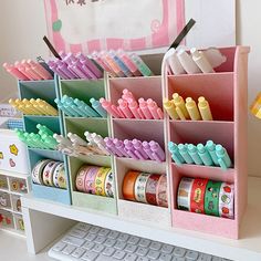 an organized desk with lots of colorful pens and pencils in bins next to a computer keyboard