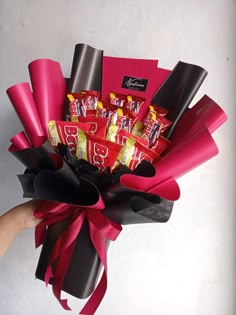 a bouquet of candy wrapped in red and black paper with a hand holding it up