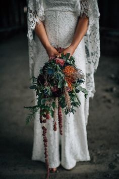 a woman in white dress holding a bouquet with flowers and greenery on the side