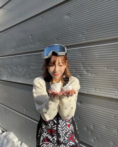 a woman standing in front of a metal wall wearing goggles and holding something up to her face