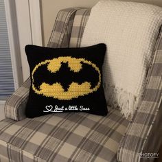 a black and yellow batman pillow sitting on top of a chair next to a window