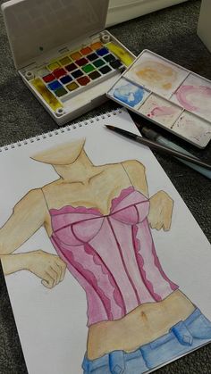 a drawing of a woman's torso with watercolor paints on the table next to it