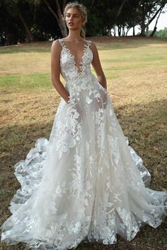 a woman wearing a white wedding dress standing in the grass with her hands on her hips