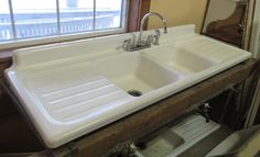 a white sink sitting under a window next to a wooden counter top with two faucets