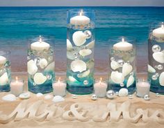 there are candles and seashells in glass vases on the beach