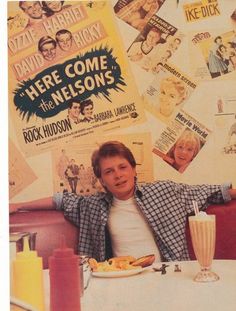 a man sitting at a table in front of a wall covered with posters and food