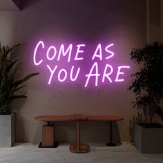 a neon sign that says come as you are on the wall next to a table