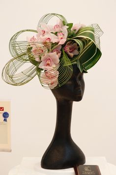 a black mannequin head with pink flowers and green leaves on top of it