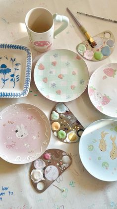 many plates and bowls are laid out on a table with paintbrushes, spoons, and other items