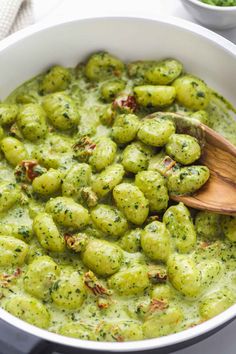 a white bowl filled with pesto gnocchini and a wooden spoon in it