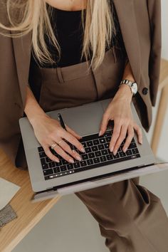 a woman is typing on her laptop while sitting at a table with a pen in her hand