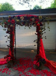 an outdoor wedding setup with red flowers and greenery on the ground next to a garage