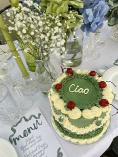 a table topped with a green and white cake next to vases filled with flowers