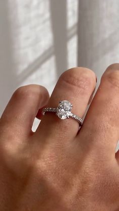 a woman's hand with a diamond ring on her finger, in front of a window