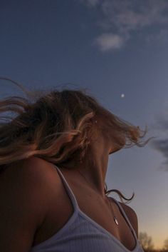 a woman with her hair blowing in the wind at sunset or dawn, looking up into the sky