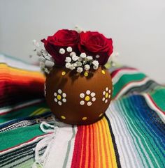 there is a vase with flowers in it sitting on a colorful blanket and striped table cloth