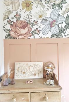 an old dresser with flowers painted on the wall behind it and other items sitting on top