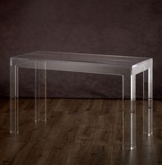 an acrylic table with clear legs on a wooden floor in front of a dark wall