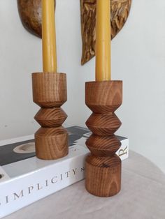 two wooden candlesticks sitting on top of a book next to a wall sculpture