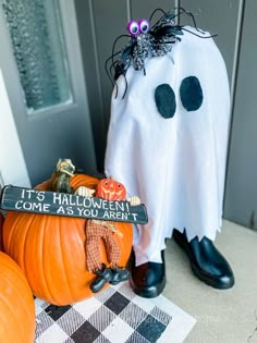 two pumpkins and a ghost sitting in front of a door with a sign that says it's halloween come as you aren