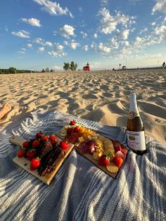 a bottle of wine and some food on a blanket in the sand at the beach