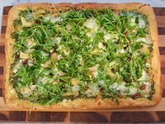 a square pizza topped with green vegetables on a wooden cutting board